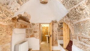 Una habitación con paredes de piedra, un banco, un radiador y una puerta de madera que da a un baño.