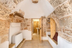 Una habitación con paredes de piedra, un banco, un radiador y una puerta de madera que da a un baño.