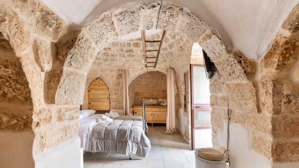 Un dormitorio con un arco de piedra, una cama, un armario de madera y una mesita.