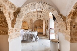 Un dormitorio con un arco de piedra, una cama, un armario de madera y una mesita.