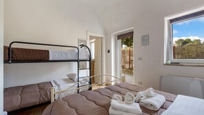 Un dormitorio tipo residencia con literas, una cama grande con toallas, un ventanal con vistas y una puerta que da a un balcón.