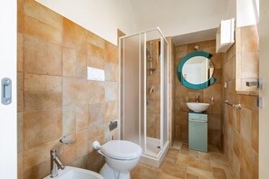 Een badkamer met douche, toilet, wastafel en spiegel.