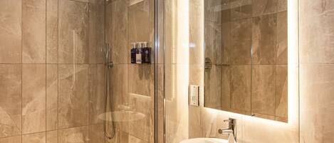 Un baño moderno con ducha envuelta en vidrio, un espejo grande y un lavabo redondo.
