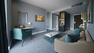 A modern hotel room with a seating area, a desk, a television, and a kitchenette.