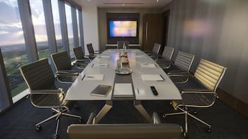 A conference room with a long table, chairs, a TV screen, and a view of the landscape through large windows.