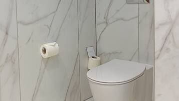 A modern bathroom with a toilet, marble walls, and a toilet paper holder.