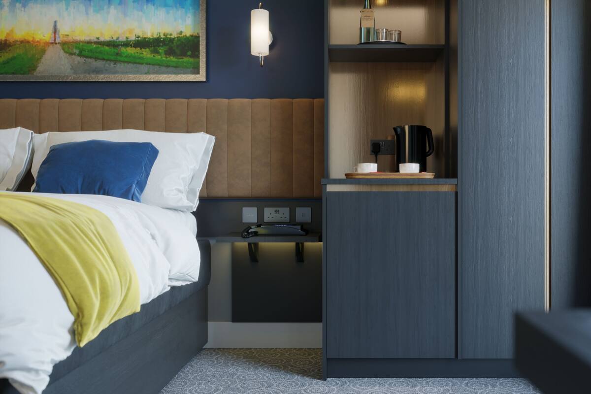 A hotel room with a bed, bedside table, and a small kitchenette area.