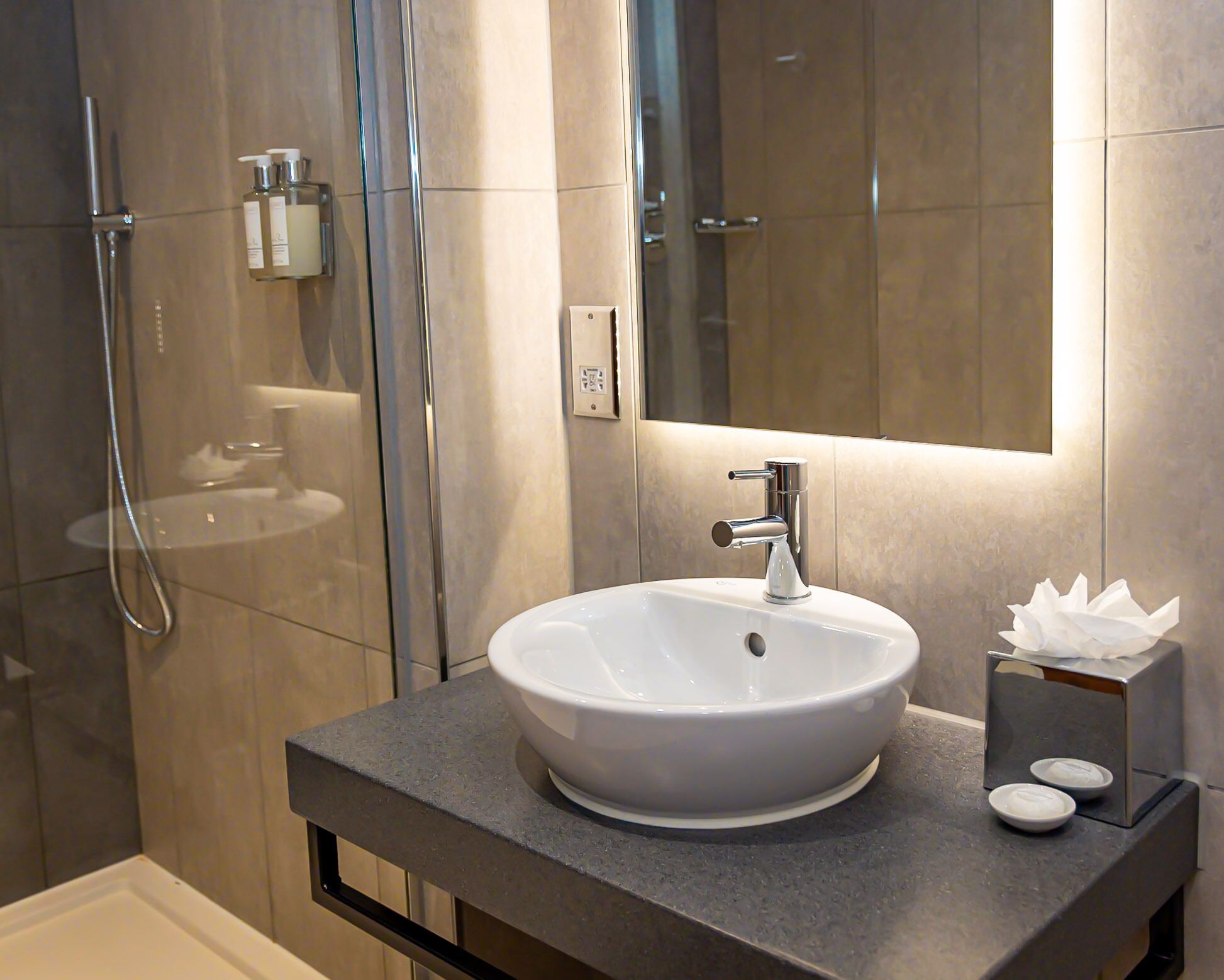 A modern bathroom with a white sink, a handheld showerhead, and a mirror.