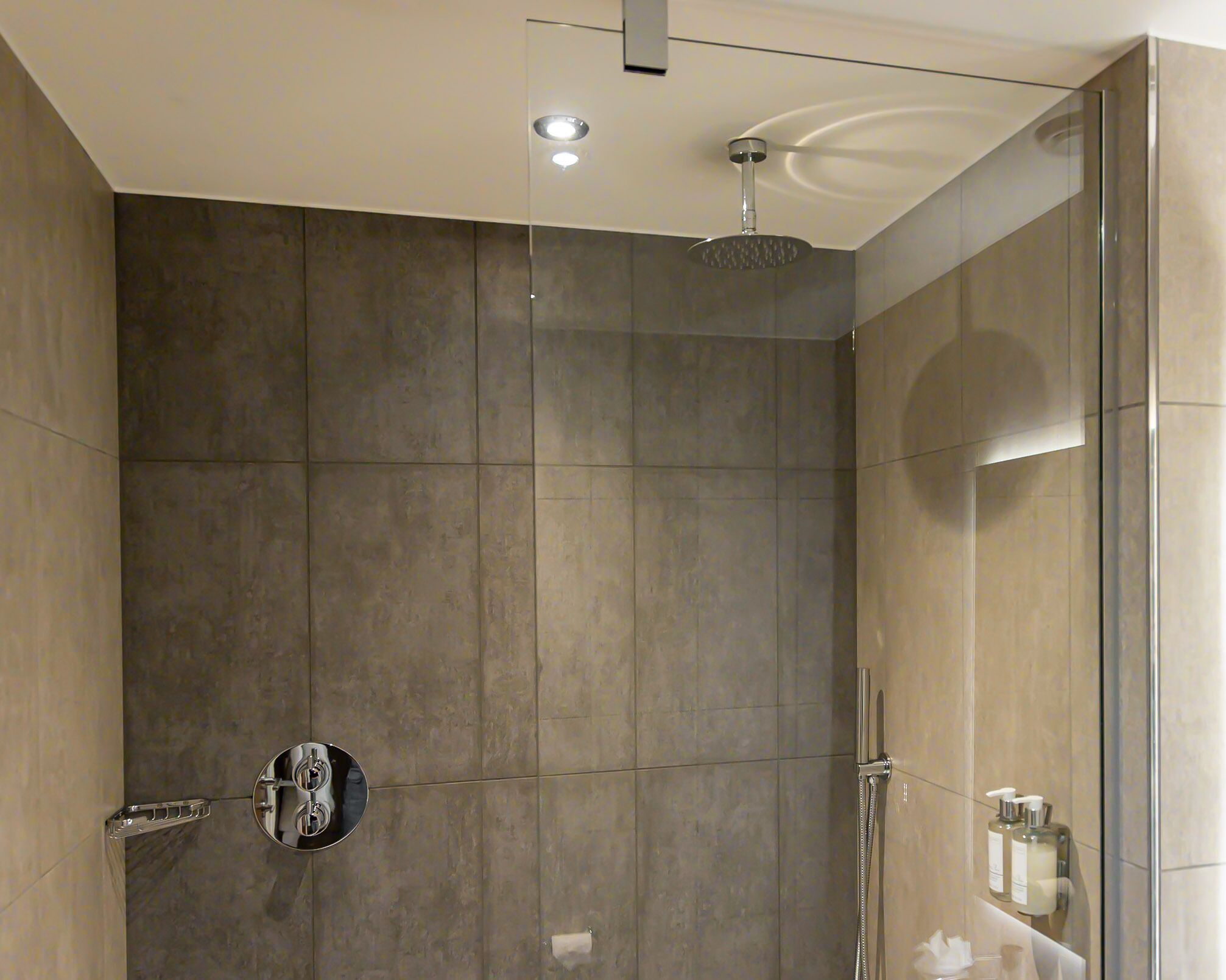 A modern shower area with a glass enclosure, a handheld showerhead, and a wall-mounted faucet.