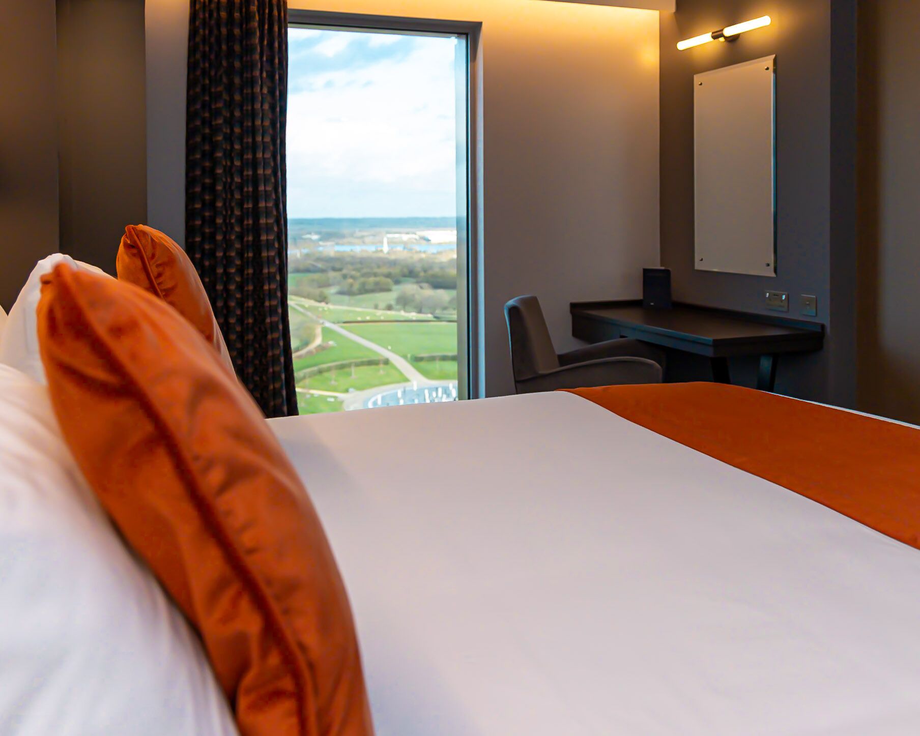 A hotel room with a large bed, a desk, and a view of a green landscape through a window.