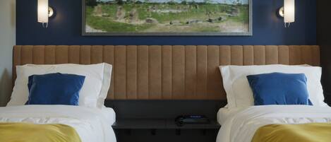 A hotel room with two beds, a headboard, a painting above the beds, and two wall sconces.