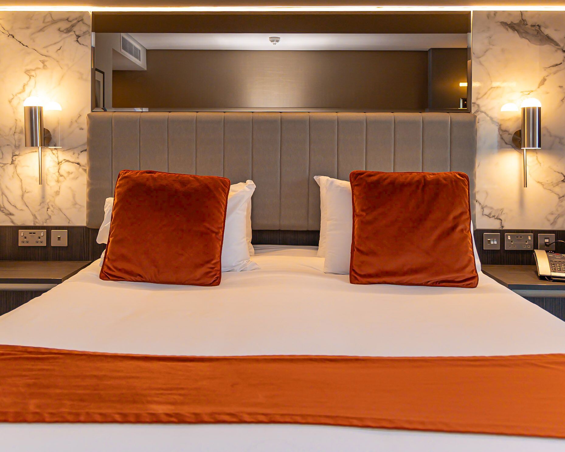 A hotel room with a large bed, two red pillows, a white bedspread, and marble-patterned walls.