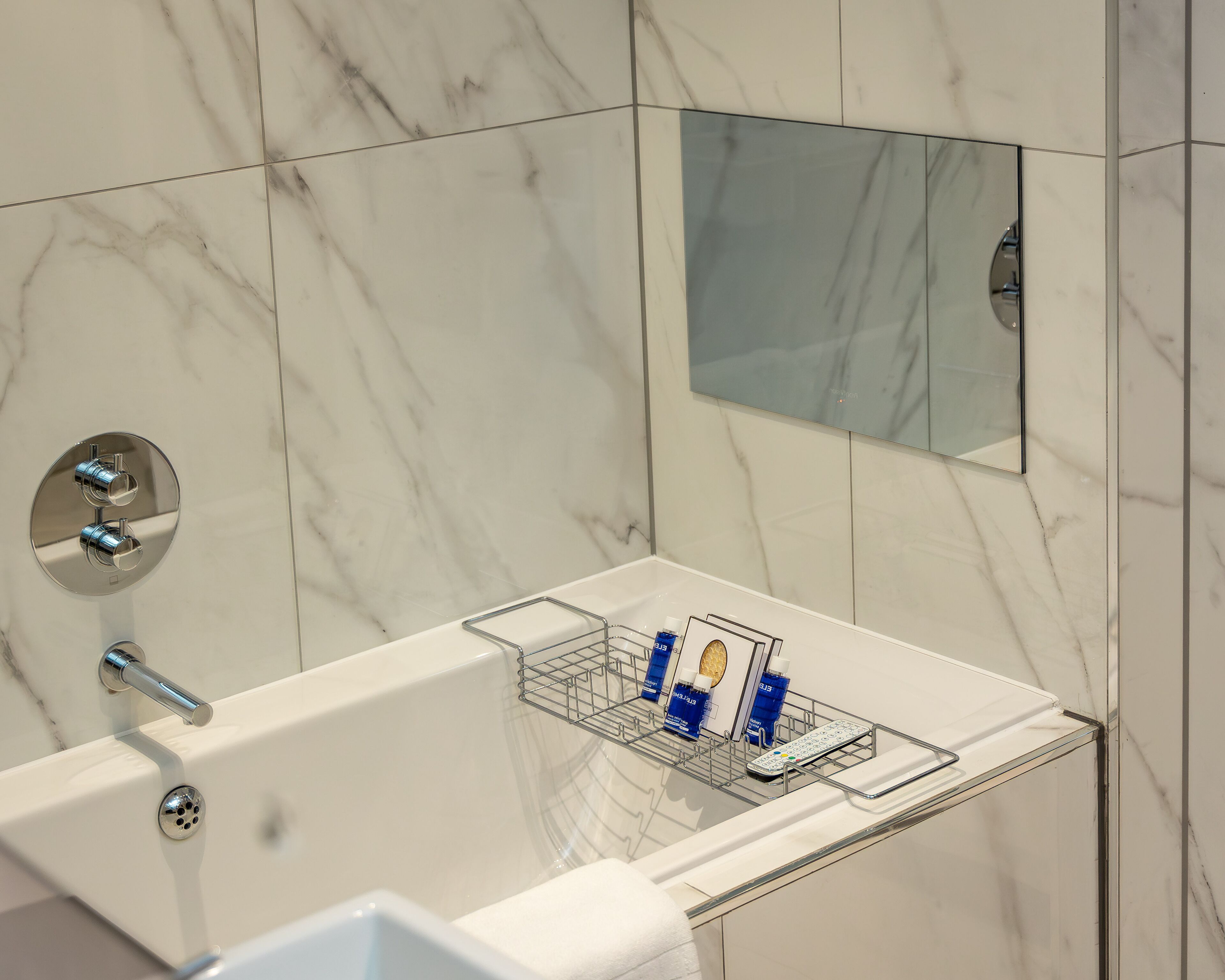 A modern bathroom with a marble wall, a glass-enclosed shower area, and a built-in mirror.