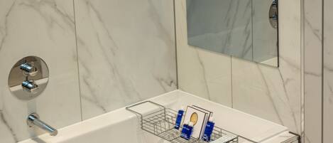 A modern bathroom with a marble wall, a glass-enclosed shower area, and a built-in mirror.