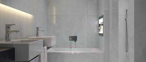 A modern bathroom with a large bathtub, two sinks, and a shower.