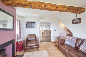 A living room with a fireplace, leather sofas, a wooden ceiling beam, and a dining area in the background. - Host & Stay | Fairview House (Ravenscar)