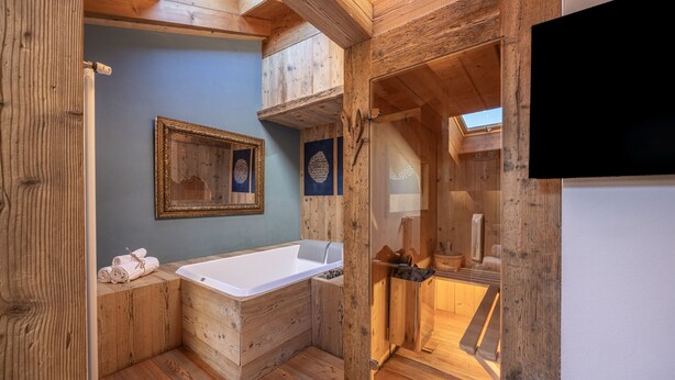 Une salle de bain rustique, située dans une cabane en bois, avec une baignoire, des murs en bois et un puits de lumière.