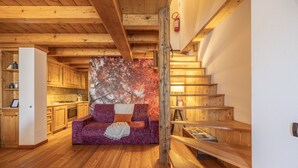 Un intérieur en bois avec un escalier, un canapé violet et un coin cuisine.