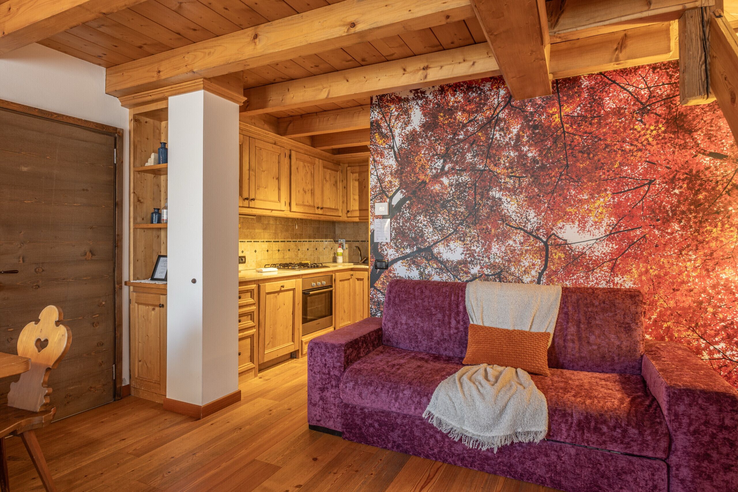 A cozy living room with a purple sofa, wooden cabinets, and a large autumn-themed wall mural.