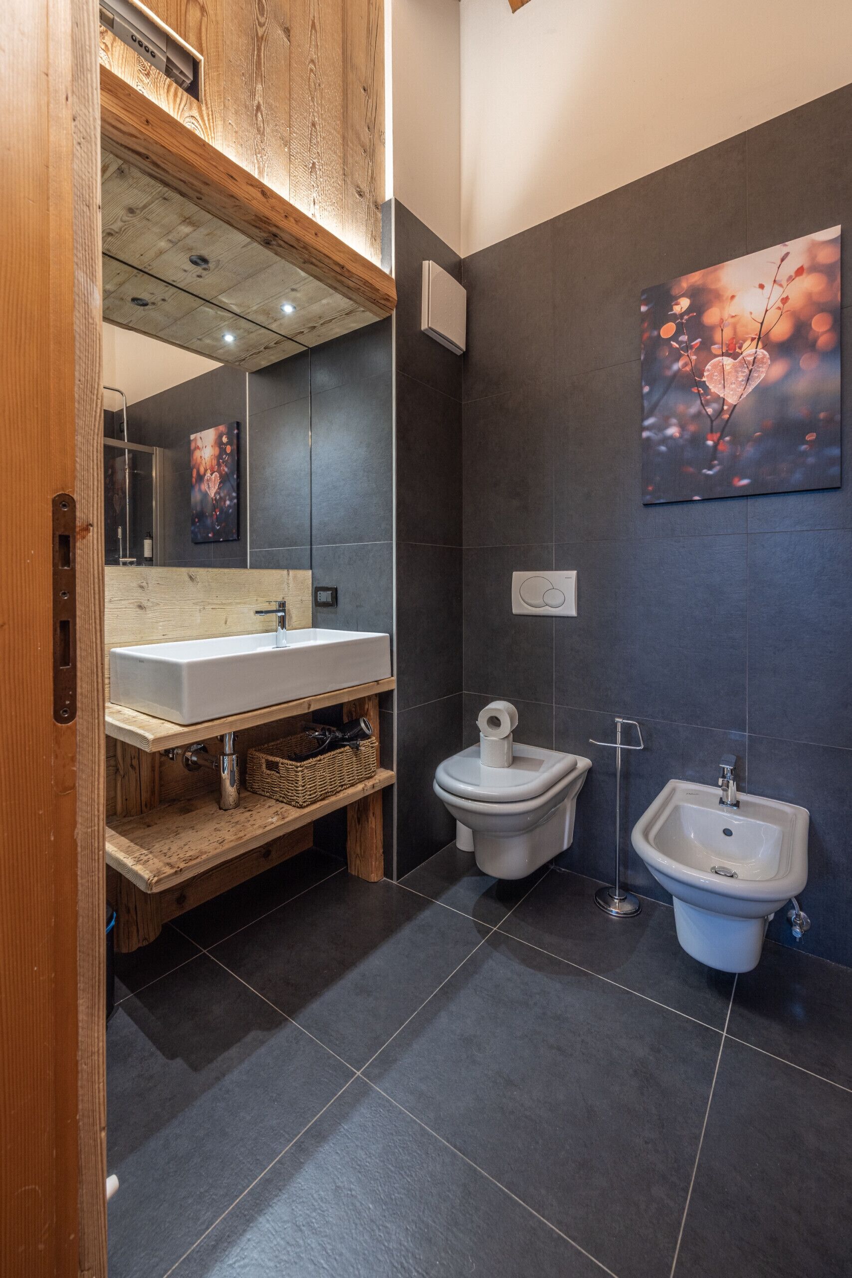 Ein modernes Badezimmer mit einem hölzernen Waschtisch, einem weißen Waschbecken, einem Bidet und einem großen Spiegel.
