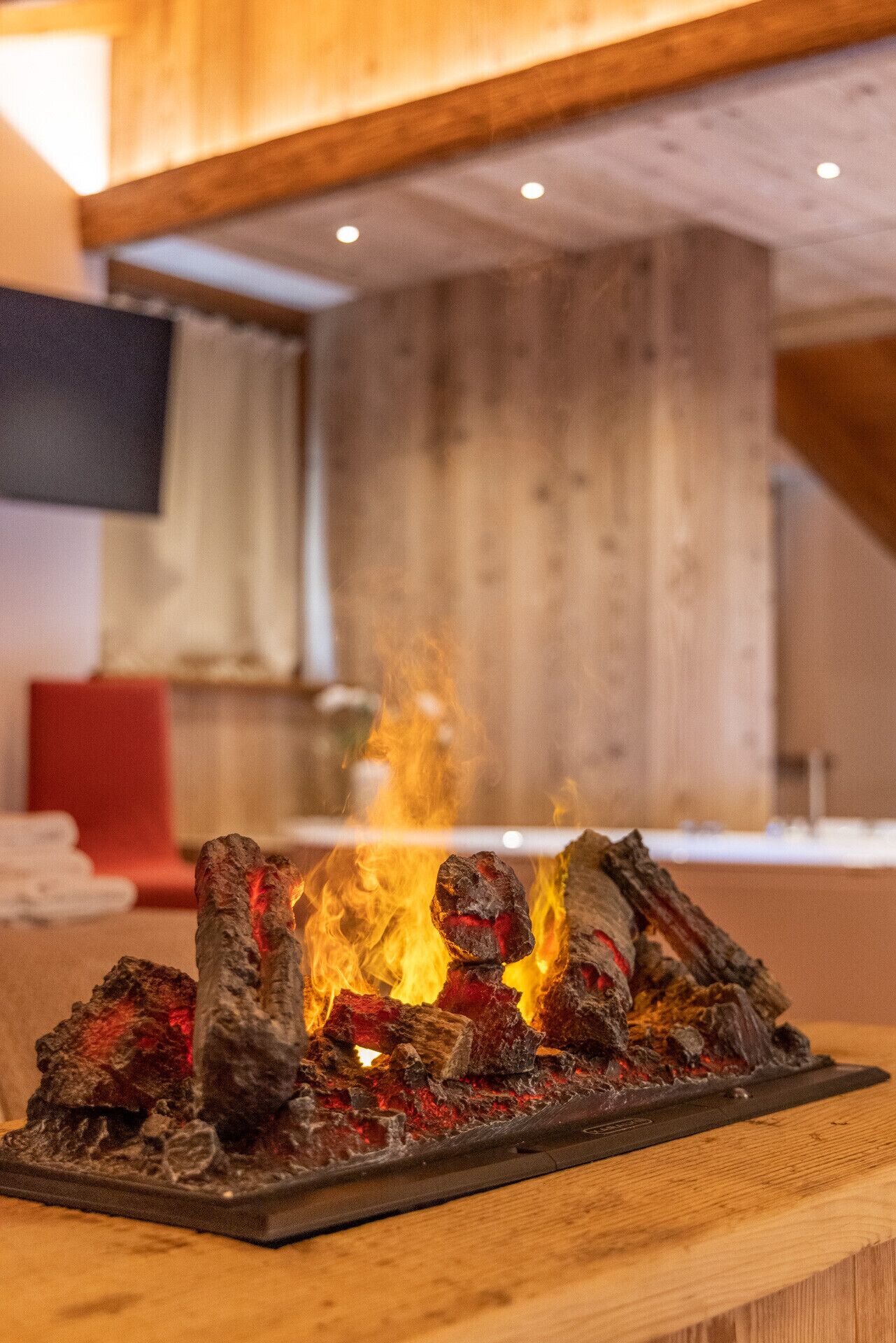 A wooden table with a charcoal grill in a room with wooden walls and a red chair.