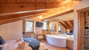 Una camera da letto mansardata accogliente con un letto grande, una vasca da bagno integrata e un soffitto in legno.