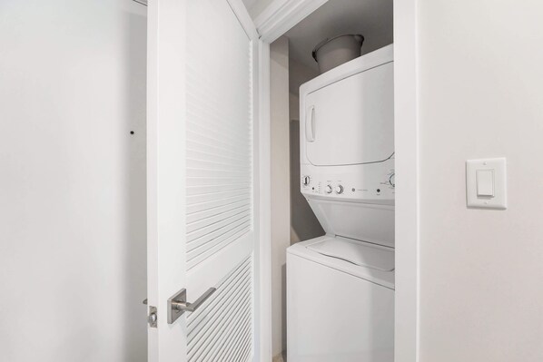 A laundry room with stacked washers and dryers, a white door, and a light switch on the wall.