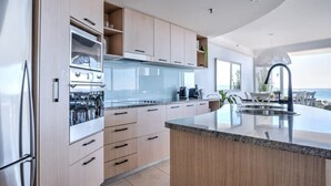 A modern kitchen with a large island, built-in appliances, and a view of the ocean. - Panoramic Ocean Views At Maroochydore (Maroochydore Region)