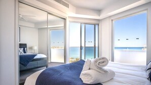A modern hotel room with a large bed, a view of the sea, and a sliding glass door leading to a balcony. - Panoramic Ocean Views At Maroochydore (Maroochydore Region)