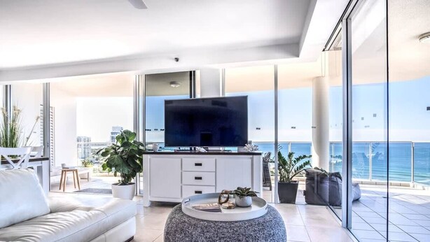 A modern living room with a sofa, a round coffee table, and a flat-screen TV. - Panoramic Ocean Views At Maroochydore (Maroochydore Region)