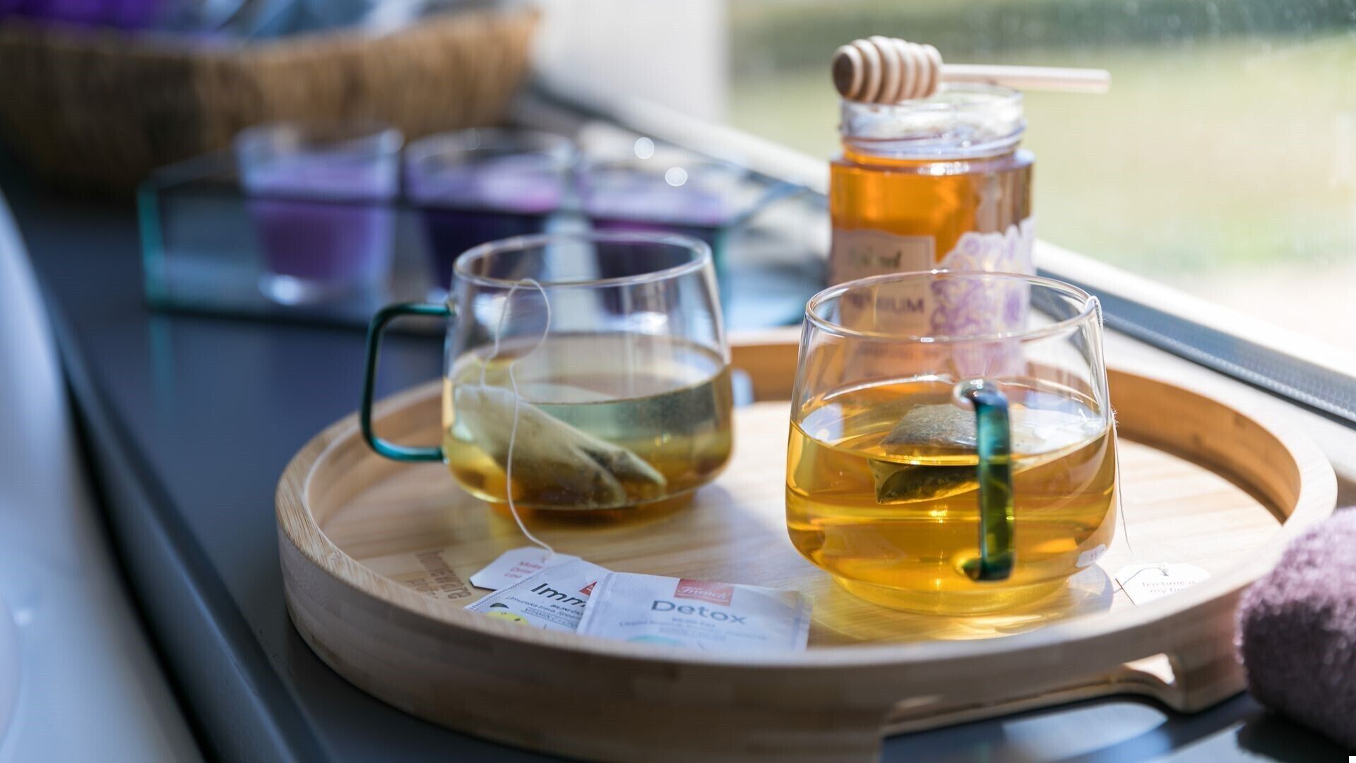 Two glasses of tea on a tray with a honey dipper and a honey jar.