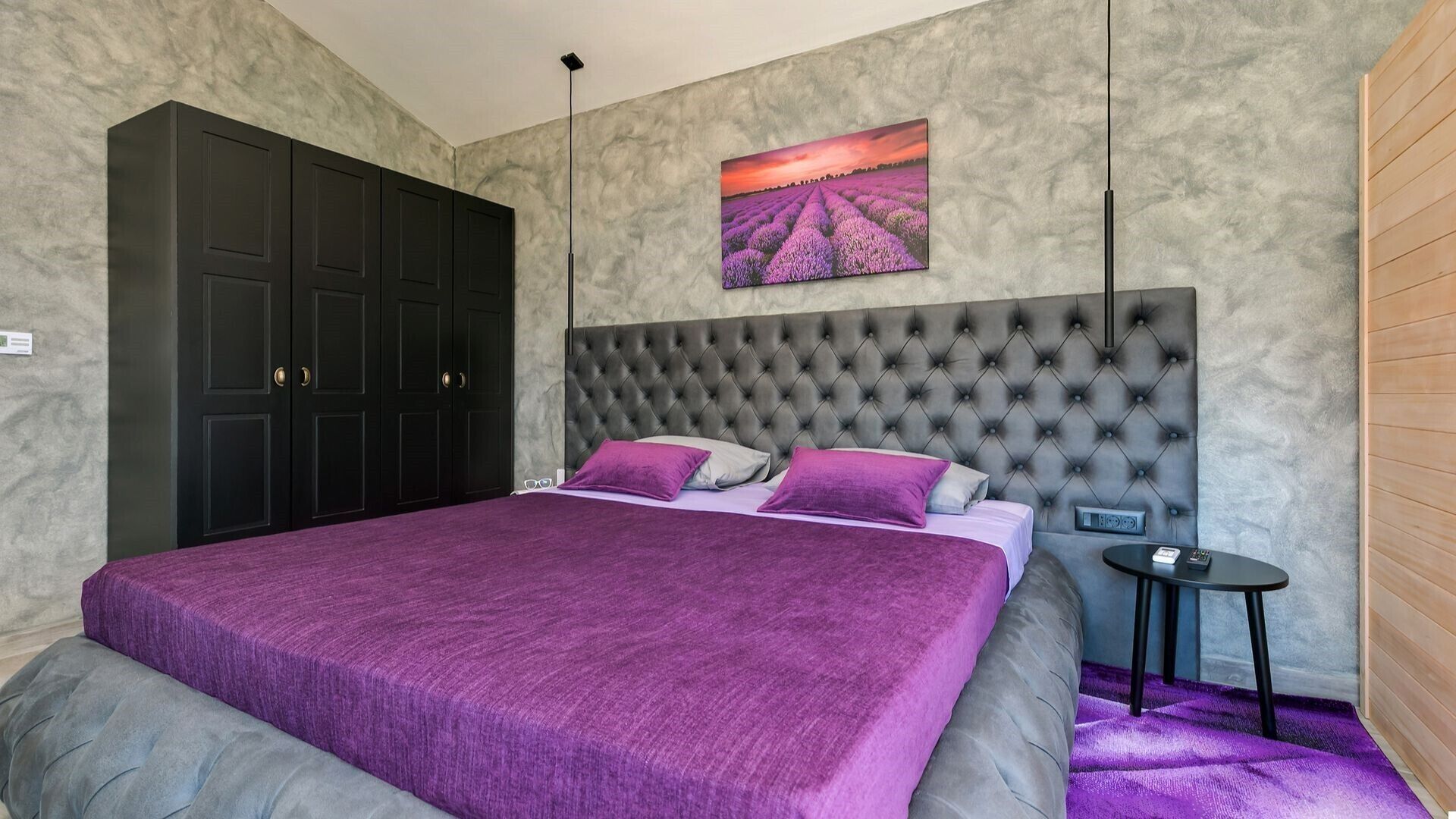 A bedroom with a large bed, a headboard, a nightstand, and a painting on the wall.