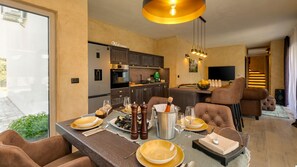 A modern dining area with a table set for four, a kitchen in the background, and a living area with a sofa and a TV. - Lovely Villa Maslina with a pool (Nova Vas)