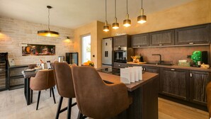 A modern kitchen with dark wood cabinets, a central island with bar stools, pendant lighting, and a wine display. - Lovely Villa Maslina with a pool (Nova Vas)