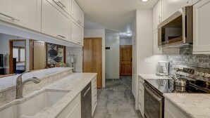 A modern kitchen with white cabinetry, a marble countertop, and a built-in oven. - Newly Remodeled Spacious 1 Bedroom 1 Condo by RedAwning (Avon)