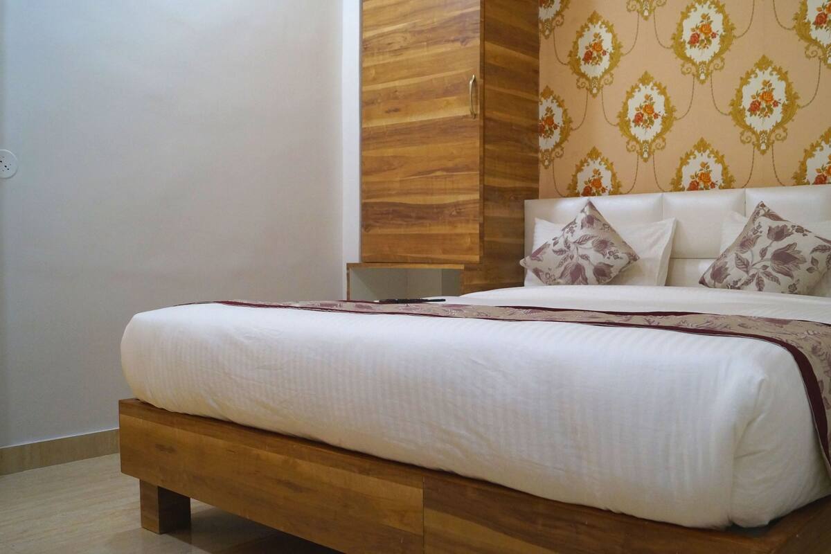 Una cama bien tendida con cabecera de madera, ropa de cama blanca y almohadas estampadas con motivos florales.