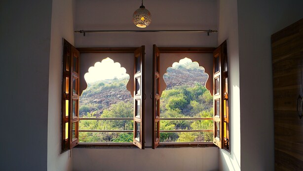 A room with two open windows featuring a decorative wooden frame and a view of a mountainous landscape. - Spring Sky Udaipur by ShriGo Hotels (Udaipur)