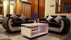 A modern living room with two dark brown sofas, a white coffee table, and a vase with blue flowers. - Spring Sky Udaipur by ShriGo Hotels (Udaipur)