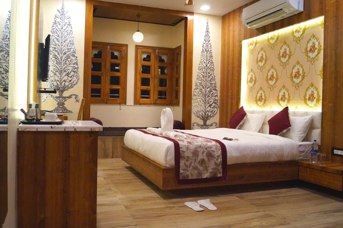Un dormitorio con cama de madera, una mesita de noche, un escritorio con una silla y una ventana con contraventanas de madera.