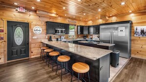 Una cocina estilo cabaña de madera con una isla central, taburetes de bar, electrodomésticos de acero inoxidable y un detector de incendios en la puerta.