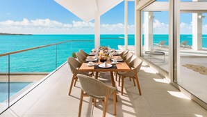 Un coin repas avec une table dressée pour quatre personnes, offrant une vue sur une mer turquoise et un ciel dégagé.