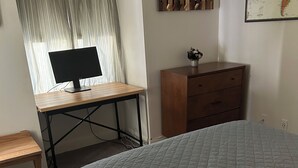Een slaapkamer met een bed, een bureau met een computer, een dressoir en een kaart aan de muur.