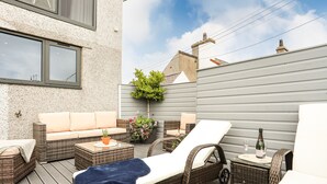 Un patio esterno con mobili in vimini, un divano imbottito, una poltrona relax e un tavolino con una bottiglia e un bicchiere.