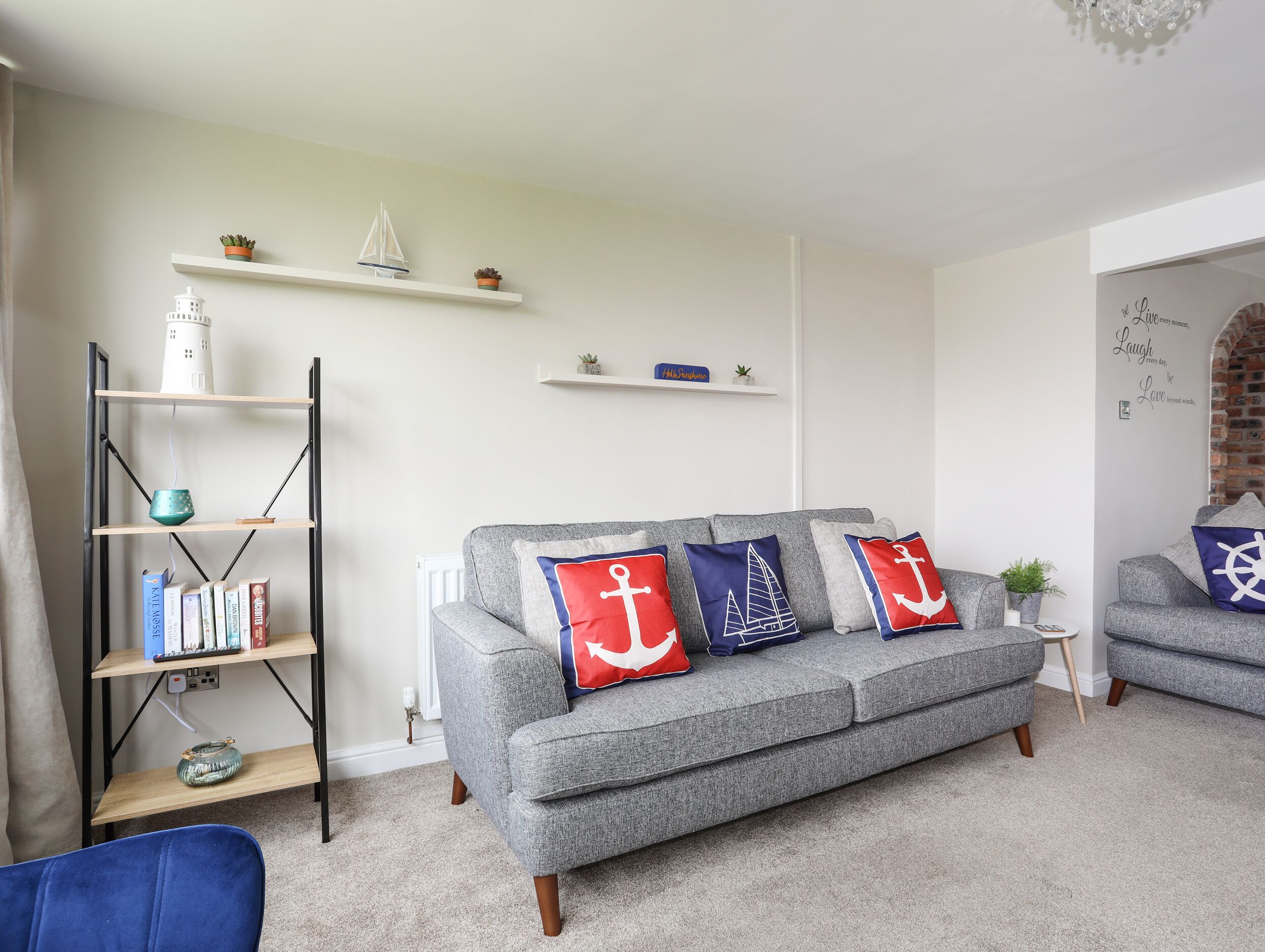 A living room with a grey sofa, bookshelves, and decorative pillows with anchor designs.