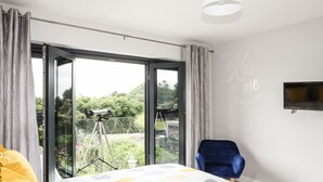 Una camera da letto con un'ampia finestra, un telescopio, una poltrona blu e un letto con copriletto fantasia.
