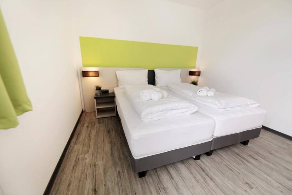 Habitación de hotel con una cama, dos mesitas de noche y una pared verde.
