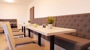 A modern, minimalist room with a long, cushioned bench along one wall, a white table with a potted plant, and a small table with a yellow cup and a salt shaker. - bp24 Hotel Eschweiler (Eschweiler)