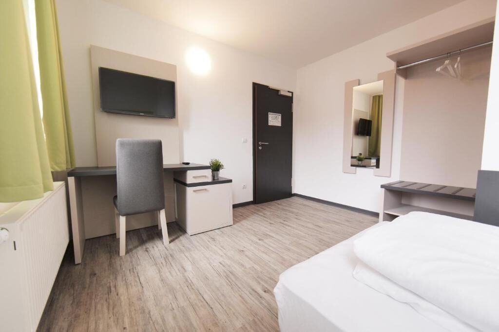 A hotel room with a bed, a desk, a chair, a television, and a door.