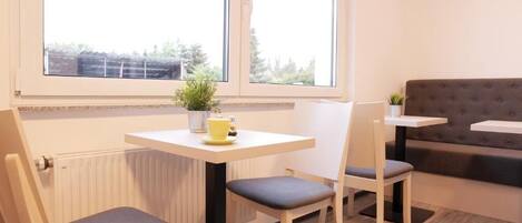 A small, bright room with a window, a radiator, a table with chairs, and a sofa.