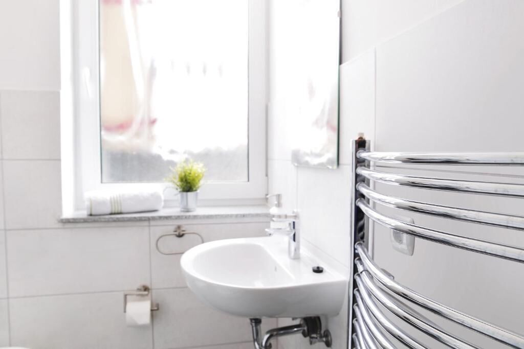 Un baño con lavamanos blanco, toallero de cromo y ventana con planta.
